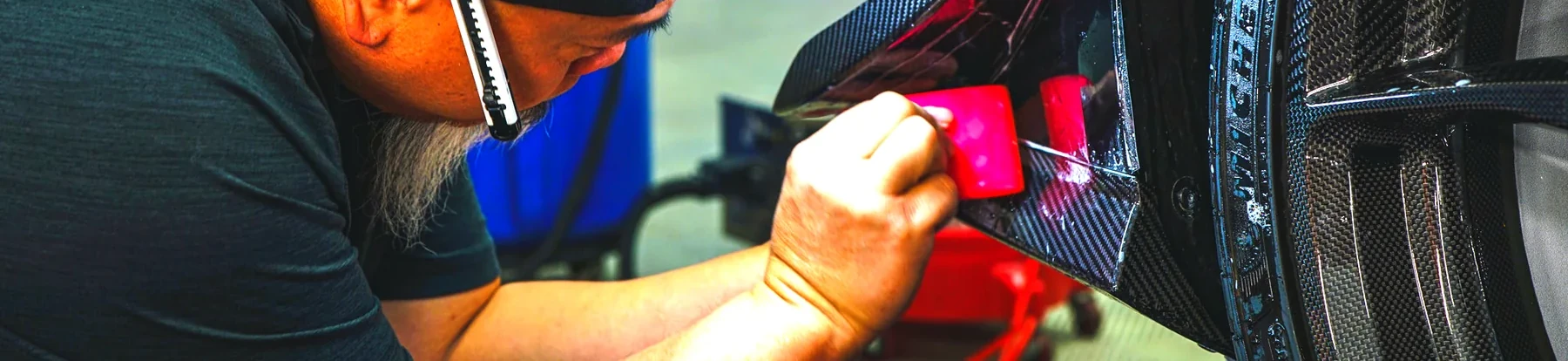 A technician laying paint protection film onto a carbon fibre wheel arch with a squeegee at Auto Obsessions